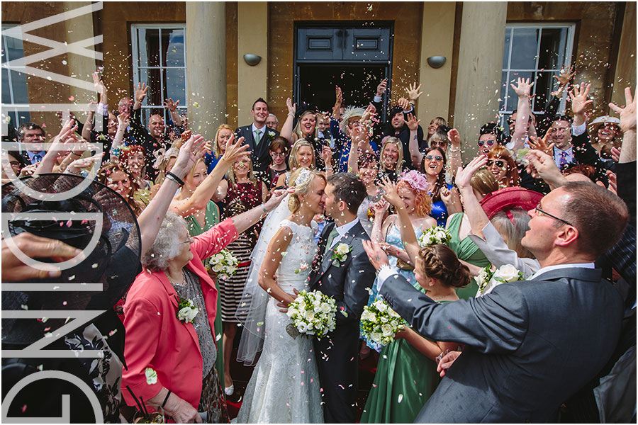 A wedding photo of a bride and groom kissing under colourful confetti after their civil ceremony on the steps of their wedding venue Rudding Park hotel and spa near Harrogate in Yorkshire