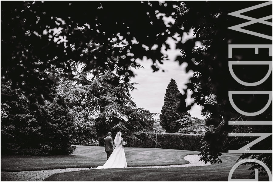 A bride and groom walk through the ornate gardens along a pretty gravel path at their wedding at Goldsborough Hall Stately House between Harrogate and Knaresborough in North Yorkshire