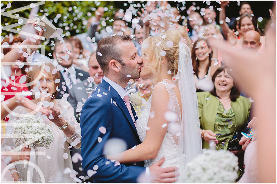 A bride and groom kiss under colourful confetti at their wedding at The Saddleworth Hotel near Oldham in Lancashire