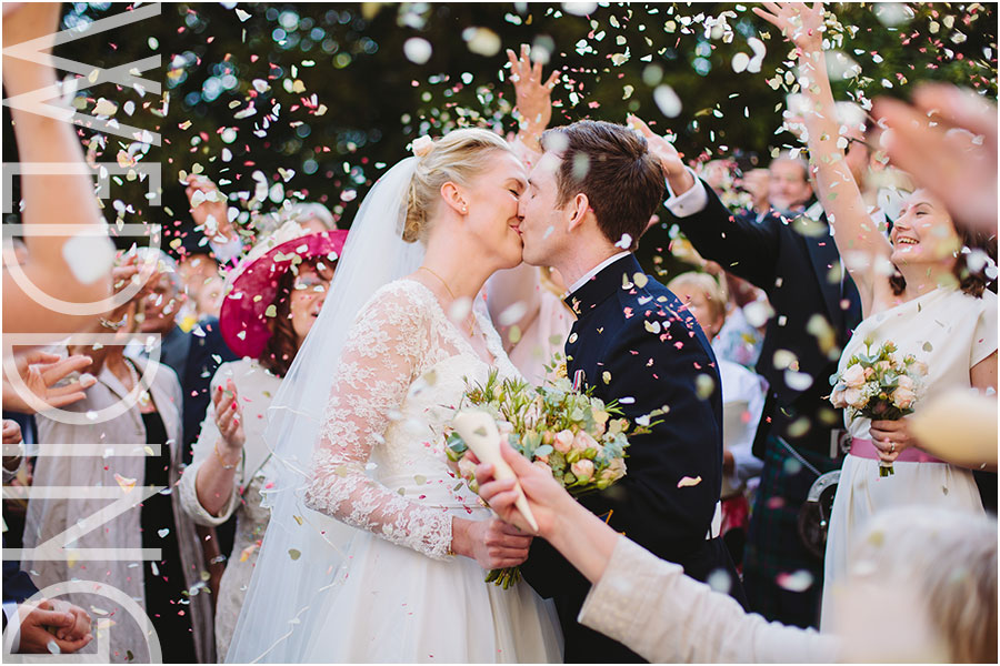 A bride and military groom kiss under colourful confetti at their wedding at Goldsborough Hall stately home between Harrogate and Knaresborough in North Yorkshire