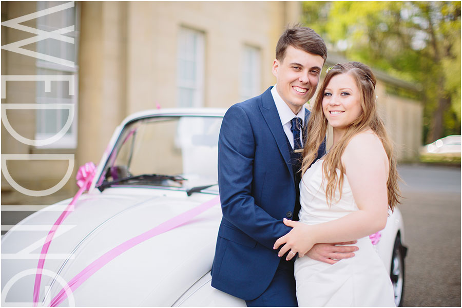 A bride and groom pose for relaxed wedding photos by their VW beetle at The Mansion in Roundhay Park in Leeds in Yorkshire