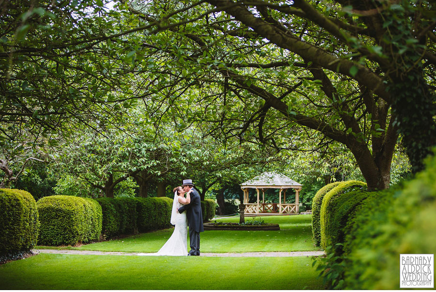 A kiss under avenue of trees at Hazlewood Castle in Top Hat and Tails at a stunning castle wedding venue in Yorkshire