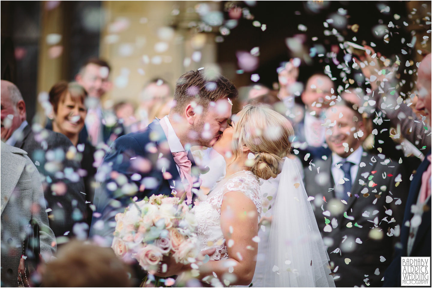 A bride and groom kiss as guests throw confetti at their wedding at The Pheasant in Harome near Helmsley in North Yorkshire