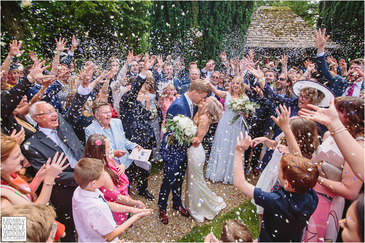 A newlywed couple kiss in a dramatic confetti photo at Hyde House in Lower Slaughter in the Cotswolds