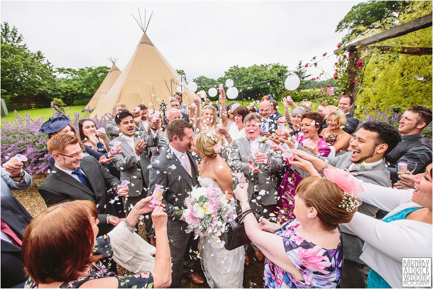 A bride and groom kiss as guests throw pink and white confetti at their wedding at The Star Inn in Harome near Helmsley in North Yorkshire