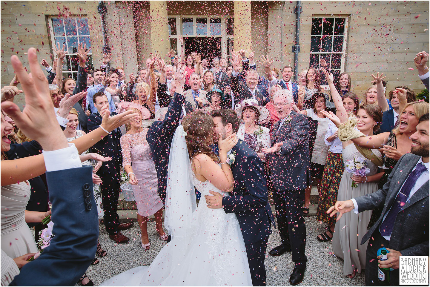 A bride and groom kiss as guests throw colourful confetti after their civil ceremony at Saltmarshe Hall stately home wedding venue in east Yorkshire