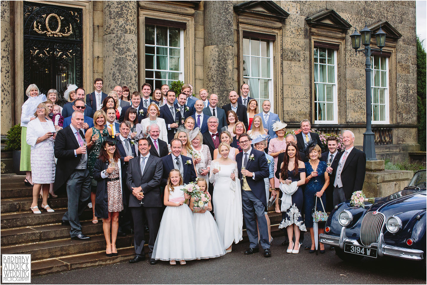 A Wedding group photograph of everyone on the stairs outside Denton Hall in Yorkshire