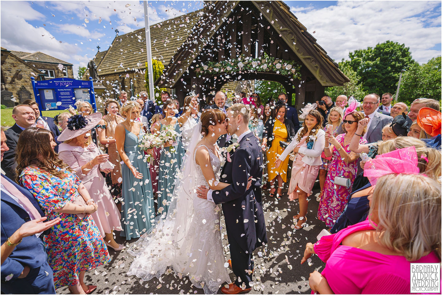 A bride and groom kiss under pastel coloured confetti outside the wedding ceremony at a church in Ilkley in Yorkshire
